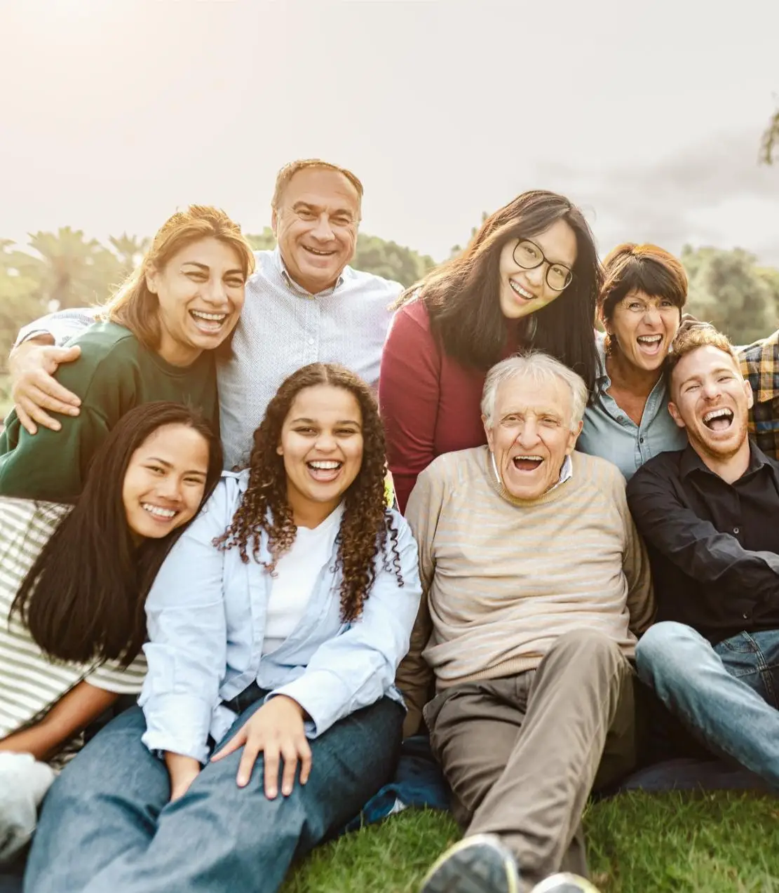 Happy multigenerational people having fun sitting on grass in a public park