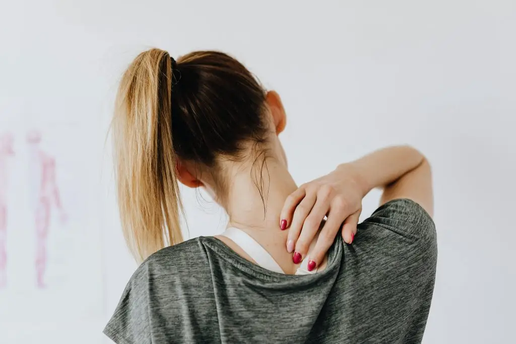 Woman gently holding her upper back with one hand, capturing the quiet tension of living with chronic pain.