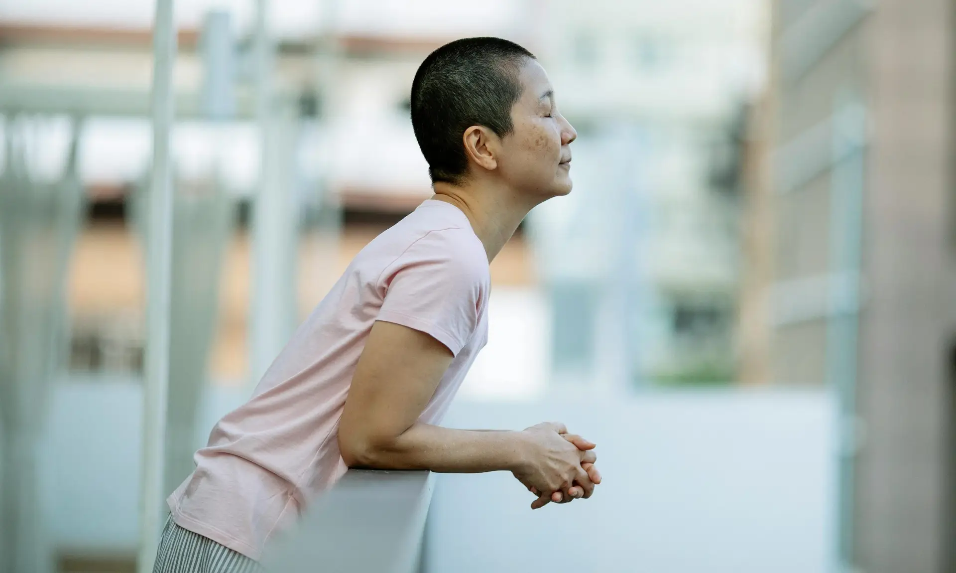 Person standing on a balcony, eyes closed and leaning on a railing, taking a deep, calming breath.