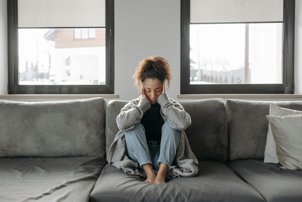 Young woman sitting on a couch with her head in her hands, looking down, appearing to be deep in thought or upset.