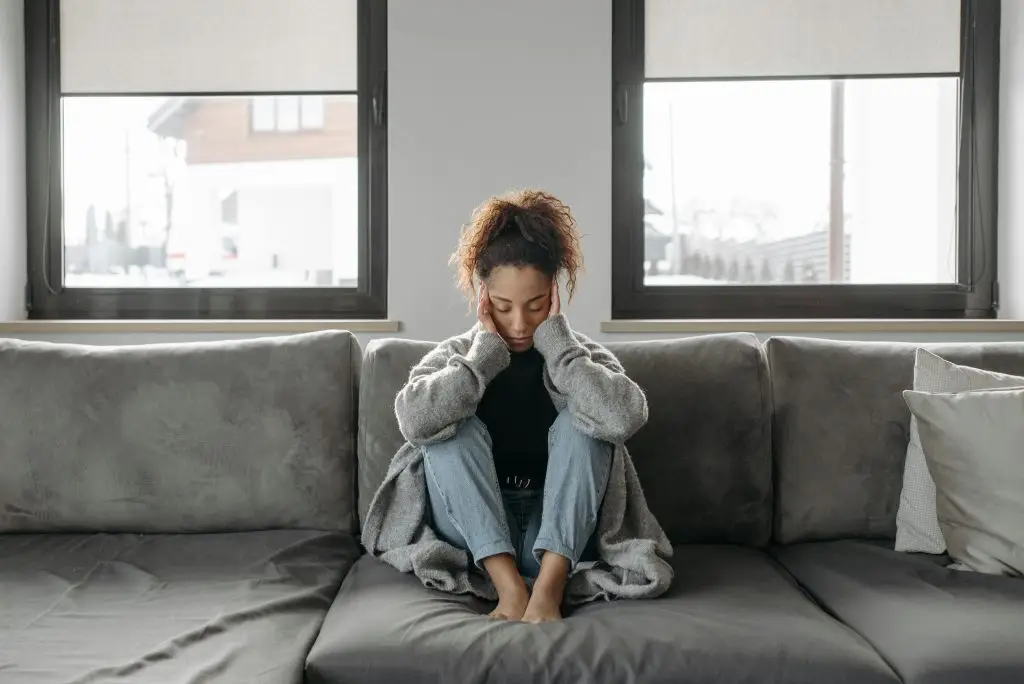 Young woman sitting on a couch with her head in her hands, looking down, appearing to be deep in thought or upset.