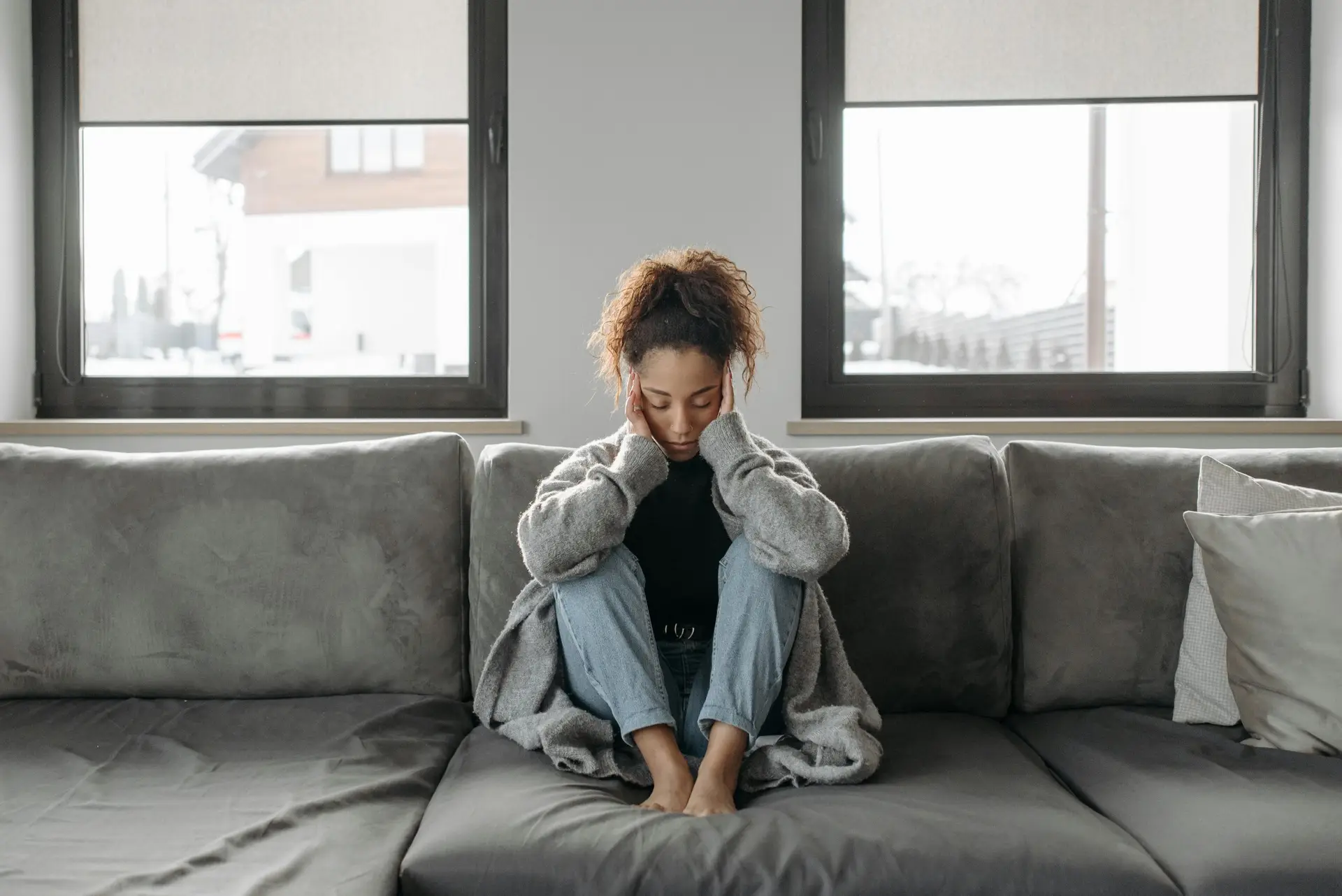 Young woman sitting on a couch with her head in her hands, looking down, appearing to be deep in thought or upset.