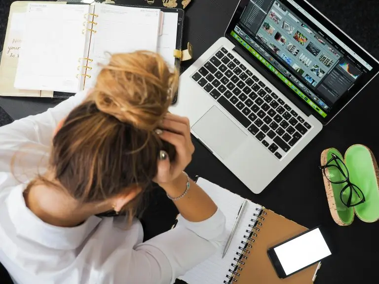 Overhead view of a stressed woman sitting at a desk with a laptop and open planner.